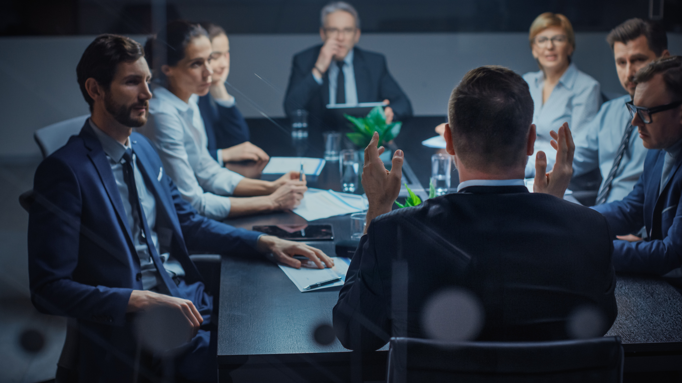 Late at Night In the Corporate Office Meeting Room: At Conference Table Executive Director Talks to a Board of Directors, Investors and Business Associates. Over the Shoulder Shot. Exclusive Solution